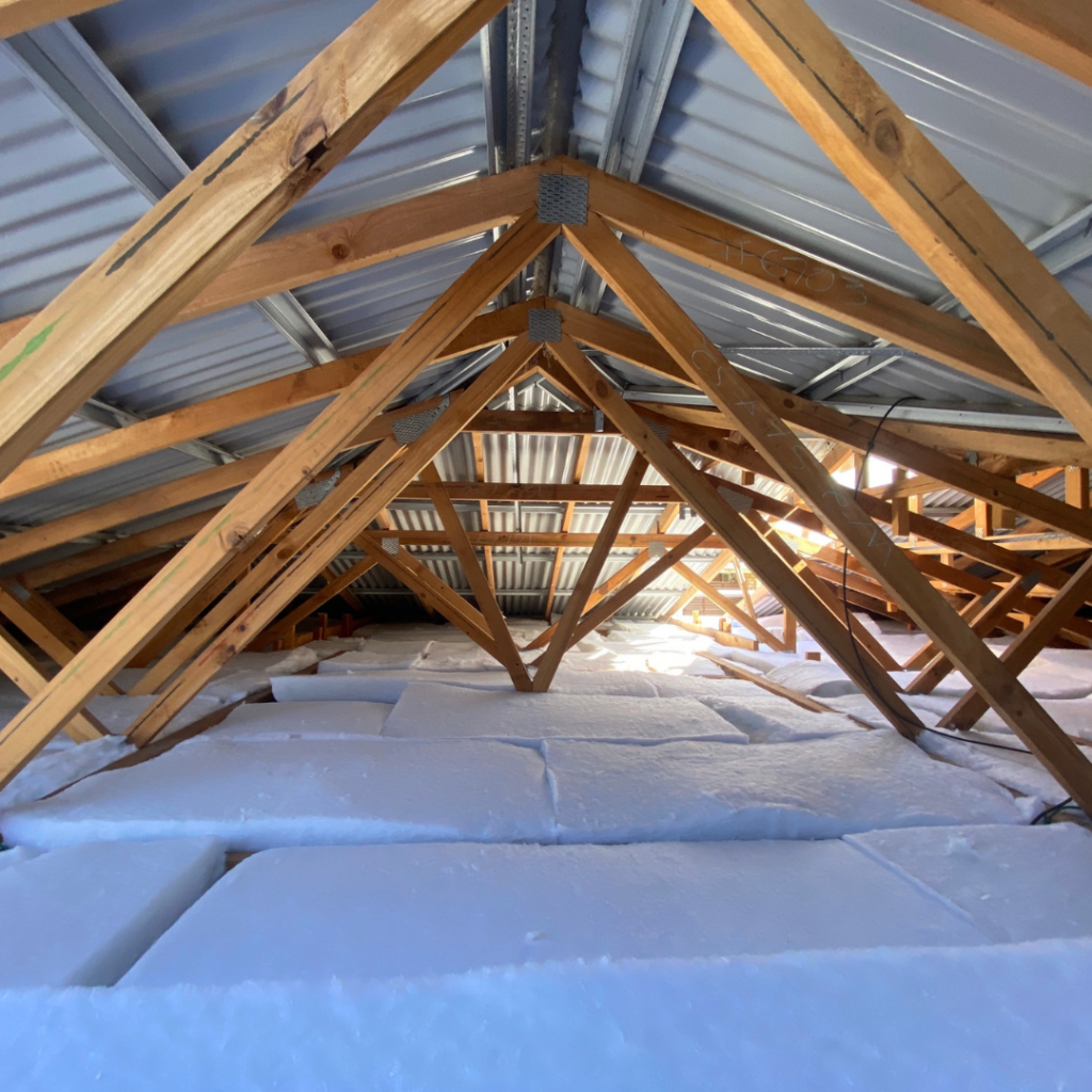 View of a well-insulated ceiling with wooden beams and structured metal roofing, showcasing thick, white ceiling insulation in a Brisbane home attic. Ideal for reducing cooling costs and enhancing comfort during Brisbane’s summer heat.